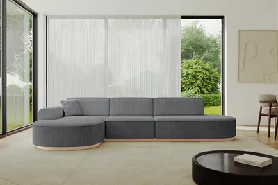 A modern living room with a large sectional sofa, large windows with sheer curtains, and a coffee table.