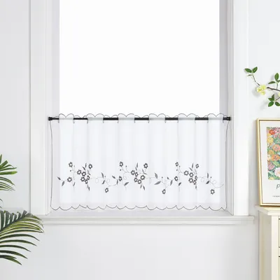 A sheer cafe curtain with a floral embroidery pattern is hung on a window.