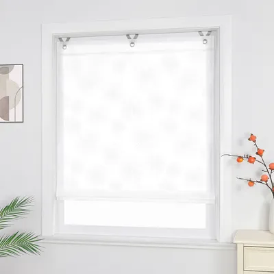 A white Roman blind with a subtle circular pattern is installed on a window. A small framed artwork hangs on the left wall, and a vase with orange berries sits on a nightstand to the right.
