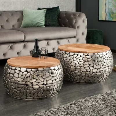 Two round coffee tables with wooden tops and mosaic-style metal bases are placed in a living room setting next to a tufted gray sofa.