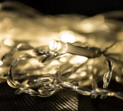 A close-up of a string of warm white LED lights with transparent wiring, resting on a textured dark surface.