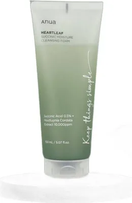 A tube of Anua Heartleaf Succinic Moisture Cleansing Foam is shown against a white and light gray background.