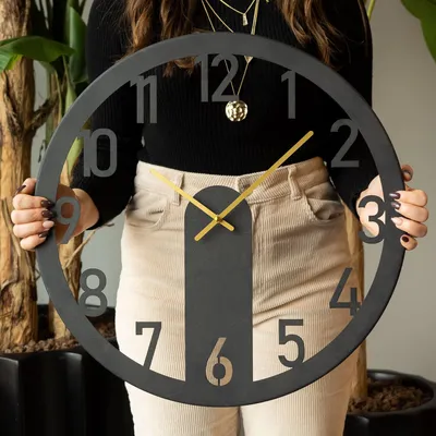 A person holding a large black wall clock with gold hands.