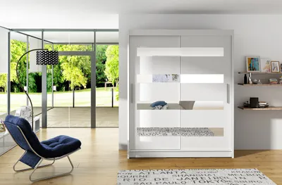 A modern living room with a large wardrobe, a blue armchair, and a floor lamp, with a view of a garden through large windows.