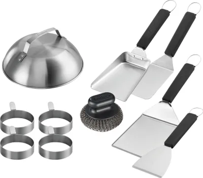 A collection of stainless steel griddle accessories, including a dome lid, spatulas, egg rings, and a cleaning brush, arranged on a white background.