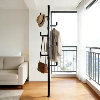 A coat rack with a hat and jacket on it, next to a sofa and a large window.