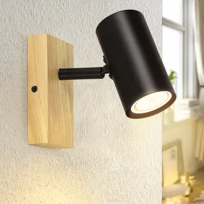 A black spotlight with a wooden base is mounted on a textured white wall.