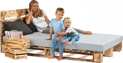A woman and two children are sitting on a bed made of wooden pallets.