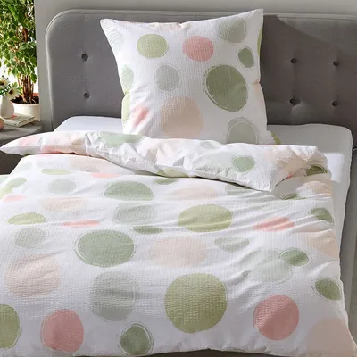 A bed with a duvet and pillow, both featuring a pattern of green, pink, and light gray circles on a white background.
