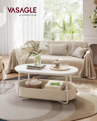 A coffee table with items on it, placed in a living room setting with a couch and plants in the background.