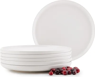 A stack of white ceramic plates with a few cranberries in the foreground.