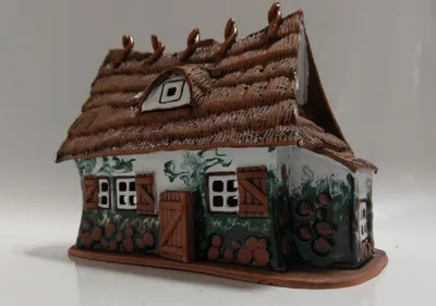 Handgefertigtes Keramikhaus mit Strohdach. Wände sind mit einem grün-weißen Muster verziert.