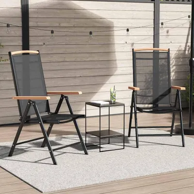 Two black folding chairs with wood accents are set up on a patio with a wooden wall in the background and string lights overhead.