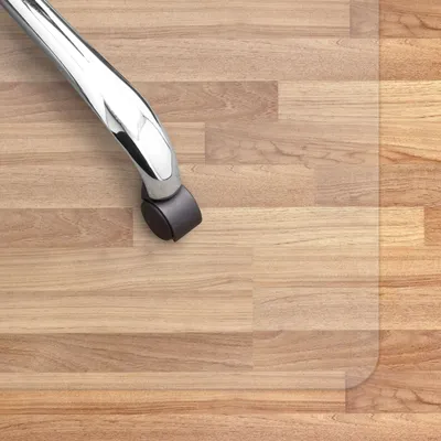 A close-up view of a chair caster on a transparent floor mat over a wood-look floor.