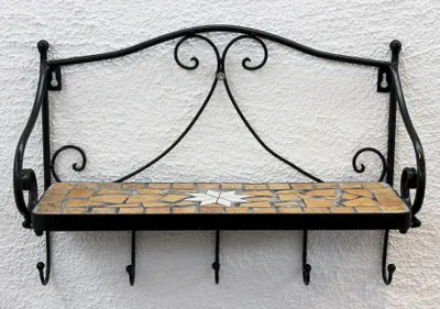 A black metal wall shelf with a mosaic tile surface and hooks underneath, mounted on a textured white wall.