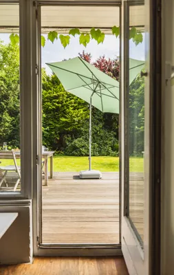 View of a garden through an open door, featuring a patio umbrella and outdoor furniture.