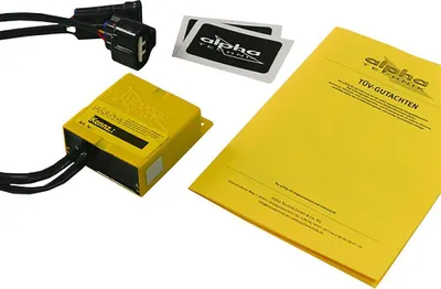 A yellow electronic control unit with cables, two stickers, and a yellow document are laid out on a white background.