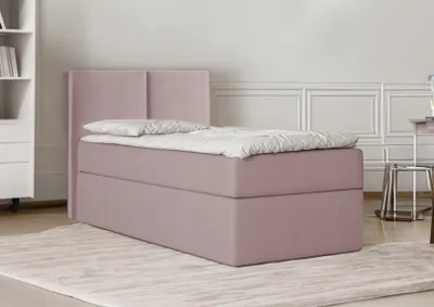 A pink box spring bed with a headboard is shown in a room with a bookshelf and a chair.