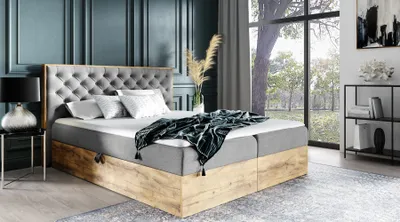 A bedroom scene with a large boxspring bed as the focal point, set against a dark blue paneled wall and a large window overlooking a garden.