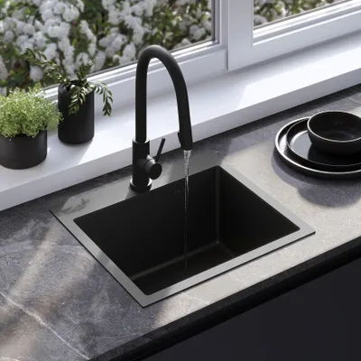 A modern kitchen sink with a black faucet and a black sink, set against a marble countertop and a window with white flowers.