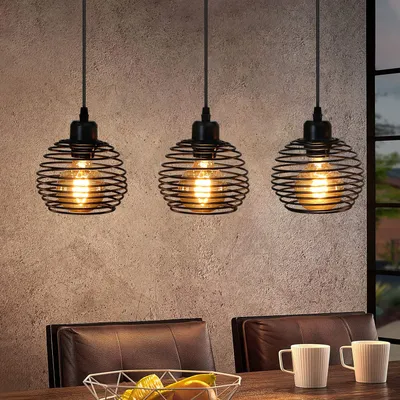 Three black metal pendant lights hang over a dining table with leather chairs and mugs.