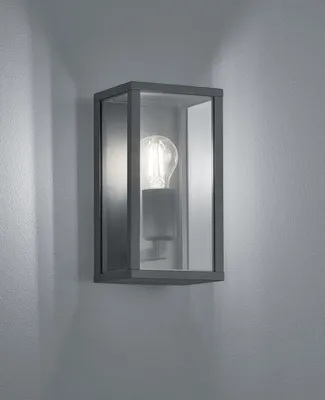 A wall-mounted light fixture with a glass enclosure and a visible light bulb, mounted on a textured gray wall.