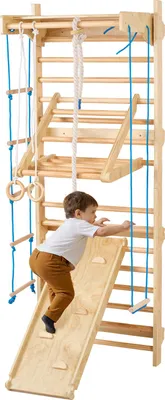 A young child is climbing on a wooden indoor gym set.
