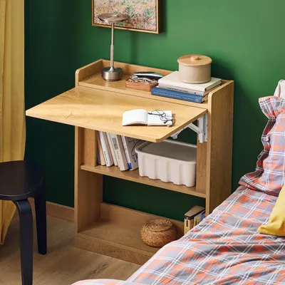 A small folding desk with shelves in a bedroom setting, next to a bed with plaid bedding.