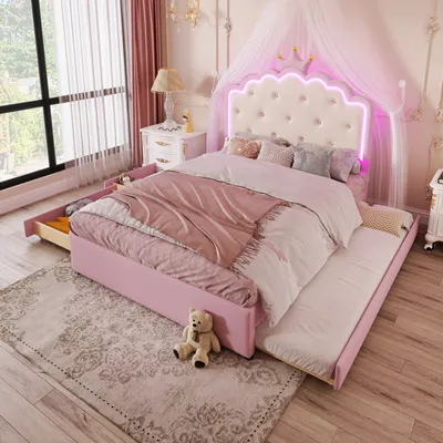 A child's bedroom with a pink upholstered bed featuring a tufted headboard with LED lighting and a crown accent, a pull-out trundle bed, and a teddy bear on a rug.