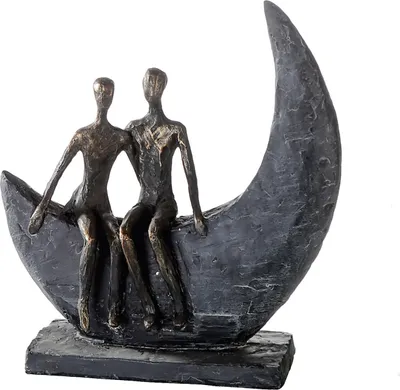 A bronze-colored sculpture of two figures sitting on a crescent moon.