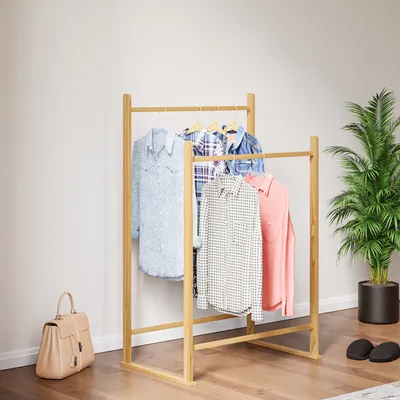 A wooden garment rack with clothes hanging on it, a handbag, and a potted plant in a room.