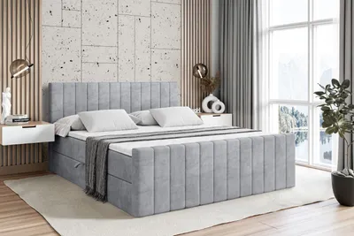 A modern bedroom with a light gray upholstered bed as the main focus, set against a textured wall and large windows.