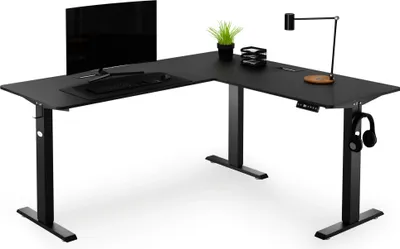 A black L-shaped standing desk with a monitor, keyboard, headphones, and a small plant.