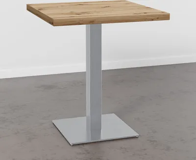 A square wooden table with a metal base against a plain wall and concrete floor.