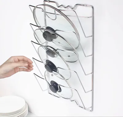 A hand reaching for a pot lid organizer mounted on a wall.