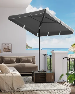 A balcony with a sofa, rug, and umbrella overlooking the ocean.