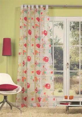 A sheer curtain with a bird print hangs in front of a window, with a chair and lamp visible.