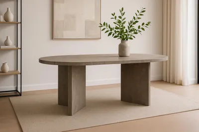 An oval dining table with a gray wood-look finish is placed on a light-colored rug in a well-lit room. A vase with green branches sits on the table.