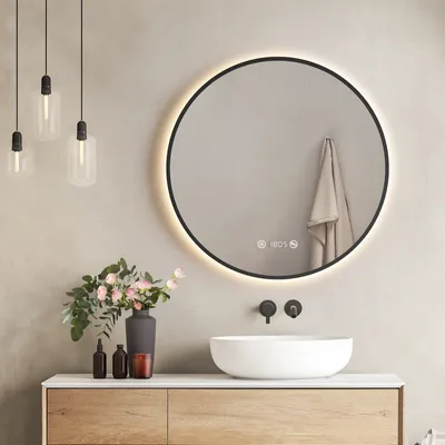 A modern bathroom vanity with a round LED mirror, sink, and decorative items.