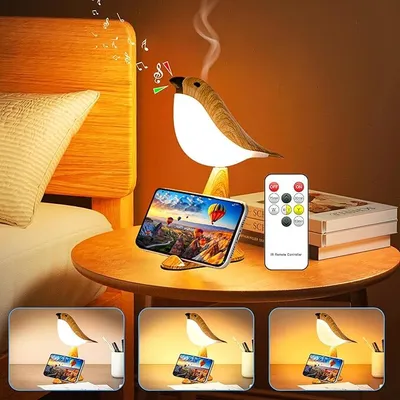 A bedside table with a bird-shaped lamp, a smartphone, a remote control, and books.