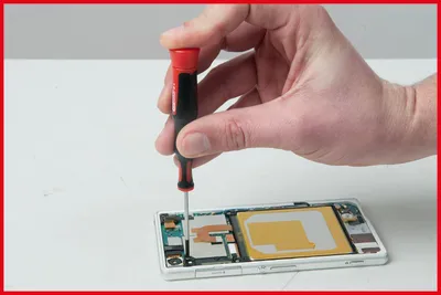 A hand is using a screwdriver to work on the internal components of a disassembled smartphone.