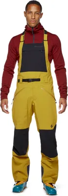 Mann trägt die Recon Stretch Bib Latzhose von Black Diamond in Gelb und Schwarz; geeignet für Herren; mit isolierenden Eigenschaften.