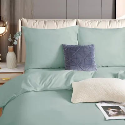 A neatly made bed with mint green bedding, pillows, and a decorative gray pillow.