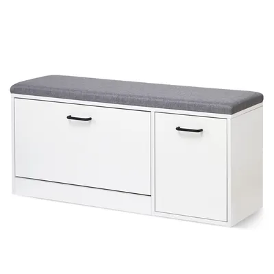 A white shoe bench with a gray upholstered seat and black handles on the doors.