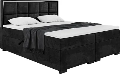 A black upholstered boxspring bed with a headboard, mattress, and topper, shown from a side-angle perspective.