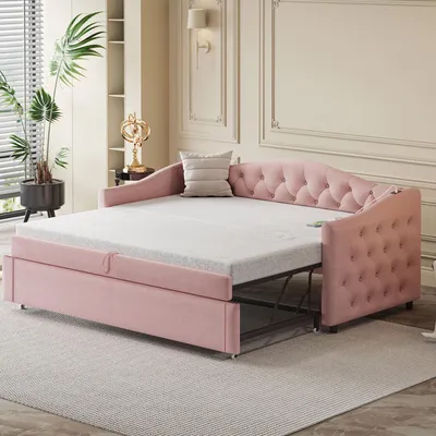 A pink upholstered daybed with a pull-out mattress is shown in a well-lit room with decorative molding on the walls and a large plant in the background.