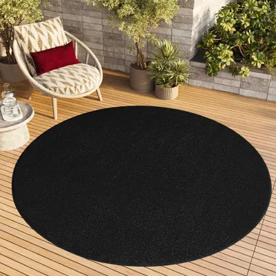 A round black rug on a wooden deck with a chair and plants.