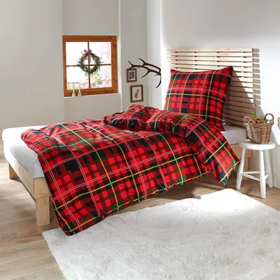 A cozy bedroom scene with a bed dressed in plaid bedding, a window with a wreath, and decorative antlers.