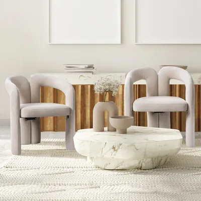 Two beige velvet chairs are placed around a marble coffee table in a living room setting.