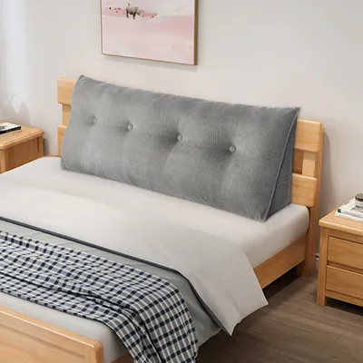 A triangular bolster pillow is placed on a bed against a wooden headboard, with bedside tables on either side.